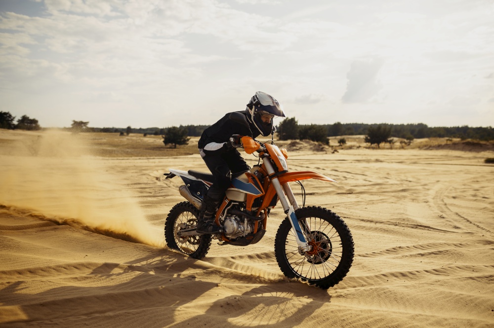 Motocross rider driving on sand dune further down off-road bike blowing dust from under wheel. Professional motocross rider driving on sand dune