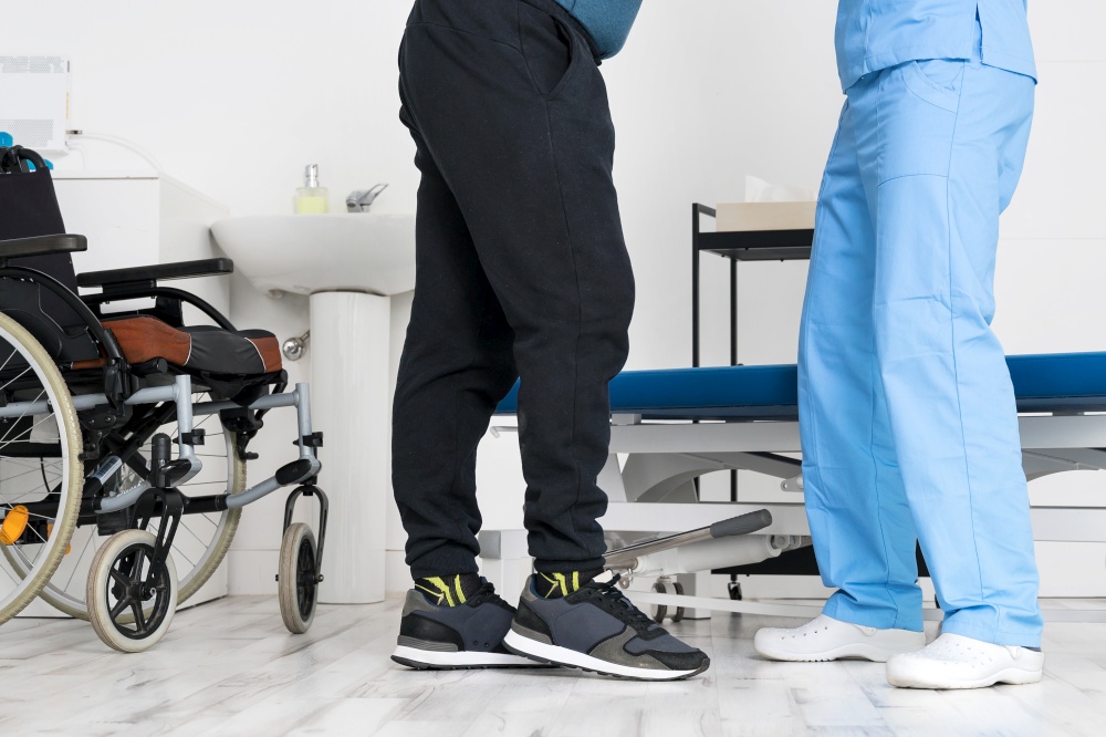 Male Physiotherapist helping a patient with a disability who uses a wheelchair, to get up at rehabilitation hospital. High quality photo.. Male Physiotherapist helping a patient with a disability who uses a wheelchair, to get up at rehabilitation hospital.