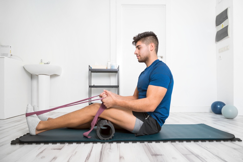 Young man Using Yoga Belt While Doing Exercise On Fitness Mat At rehabilitation clinic. High quality photo. Young man Using Yoga Belt While Doing Exercise On Fitness Mat At rehabilitation clinic.