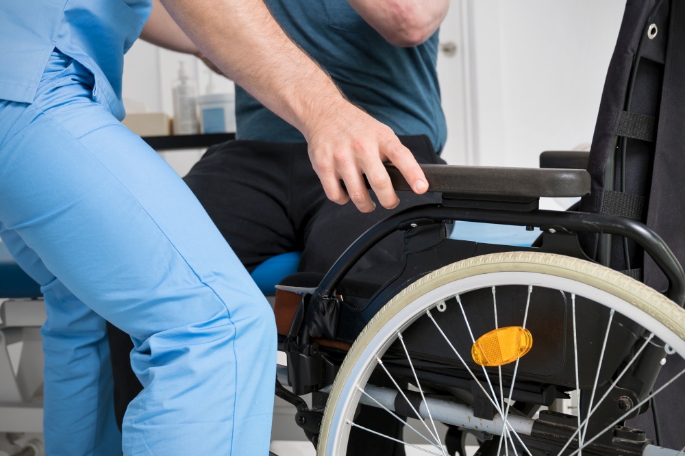 Male Physiotherapist helping a patient with a disability who uses a wheelchair to get up at rehabilitation hospital. High quality photo.. Male Physiotherapist helping a patient with a disability who uses a wheelchair to get up at rehabilitation hospital.