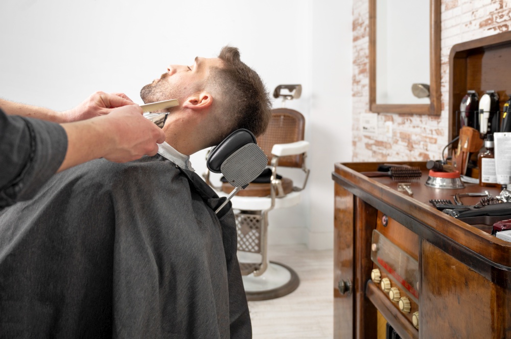 Young hipster Caucasian man during beard grooming in modern barber shop. Men&rsquo;s hair styling. Handsome man getting new hairstyle with electric trimmer. High quality photography. Young hipster Caucasian man during beard grooming in modern barber shop. Men&rsquo;s hair styling. Handsome man getting new hairstyle with electric trimmer.