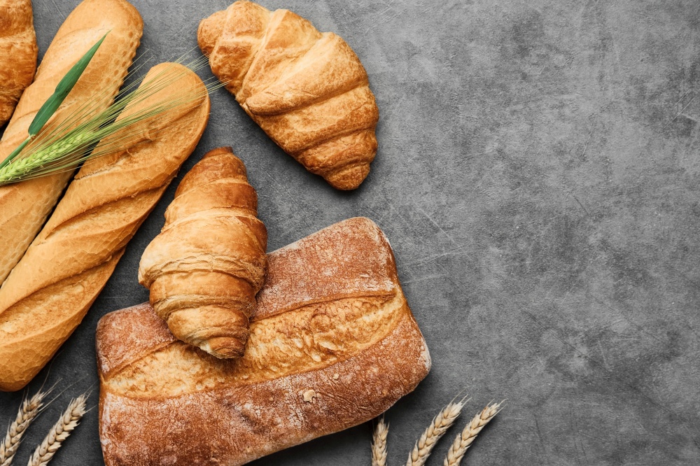 Concept of a local bakery, fresh pastries - baguette, croissant and ciabatta. Baked wheat bread lies on a gray table. Various types of freshly baked bread. Bread layout with copy space