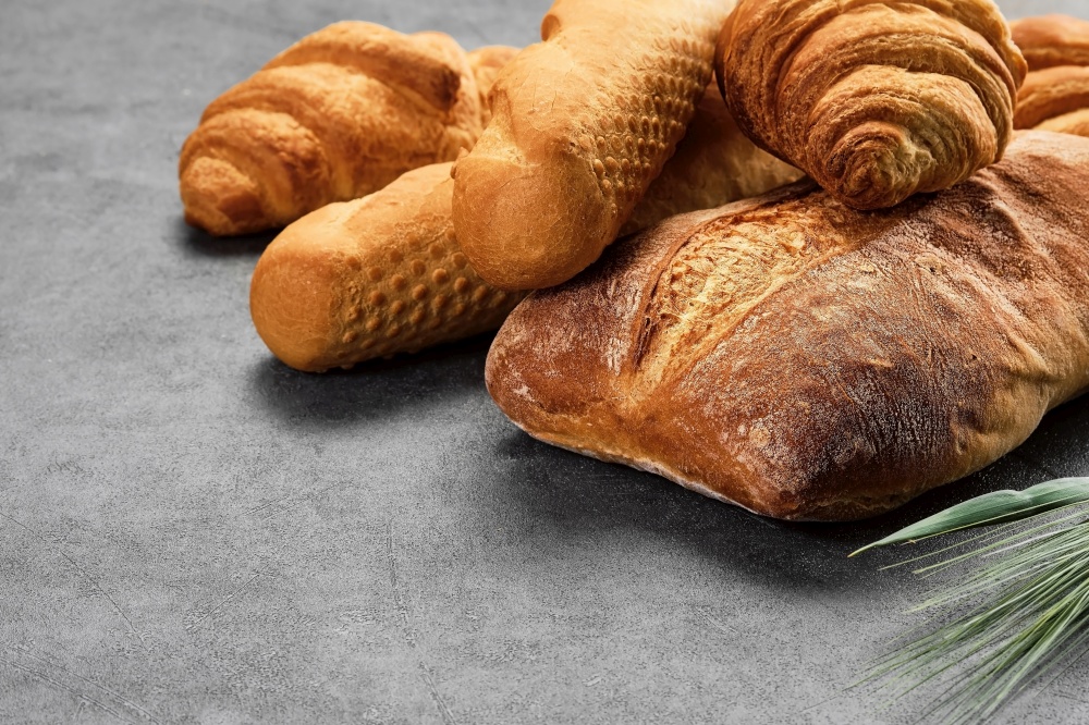 Concept of a local bakery, fresh pastries - baguette, croissant and ciabatta. Baked wheat bread lies on a gray table. Various types of freshly baked bread. Closeup with copy space