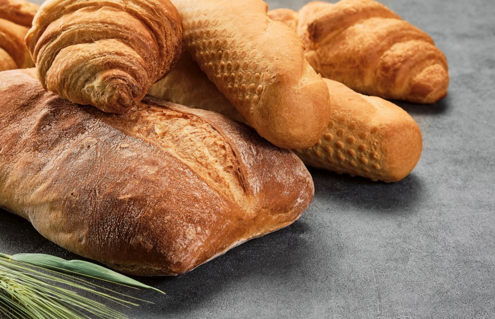 Different kinds of bread rolls on gray board, closeup. Kitchen or poster design for a local bakery. Baguette, croissant and ciabatta - various types of freshly baked bread