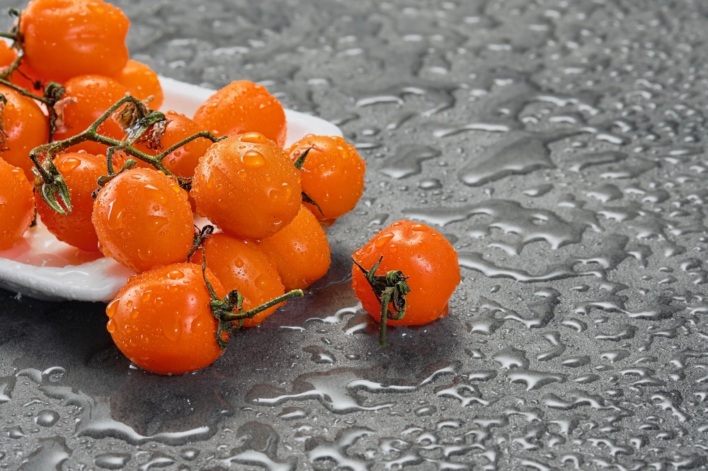 Orange cherry tomatoes in water drops on a gray table. Dark style, close-up with copy space. Ingredients for salad or dish with vegetables. selective focus