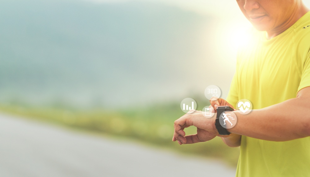 Man runner looks at a modern smart clock and counts up spent calories after training outdoors at sunset. Concept of The technology to check health while exercising.