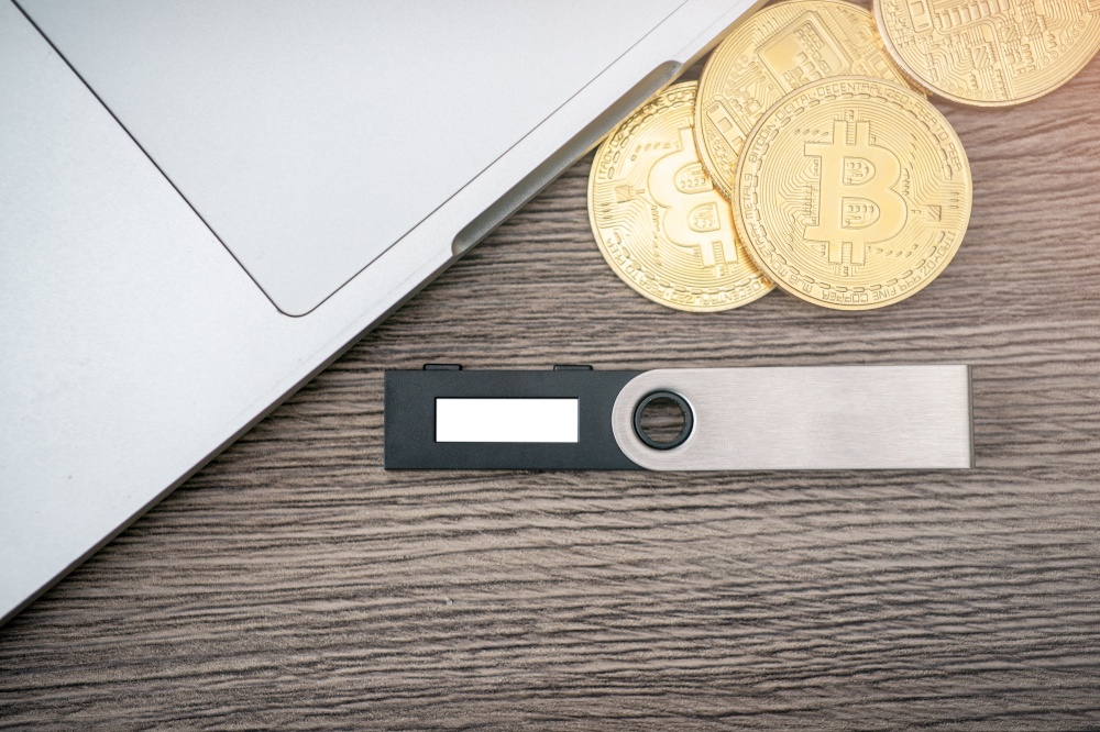 Hardware cryptocurrency wallet with golden Bitcoin (BTC) and computer. Safe storage for crypto.