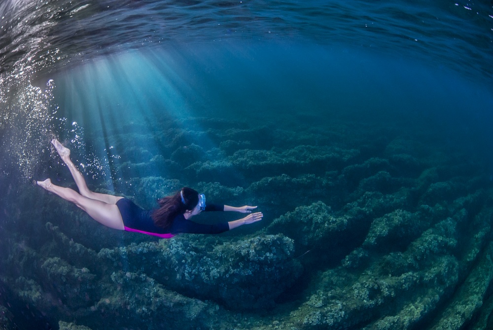 Woman swimming underwater in the Mediterranean. Rays of light entering the water from the left. . Girl snorkelling underwater in the Mediterranena sea