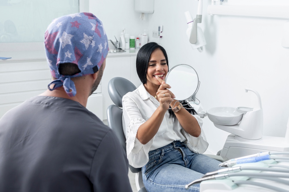 Female client smiling while looking to a mirror in a dental clinic next to a dentist. Cient smiling and looking to a mirror in a dental clinic