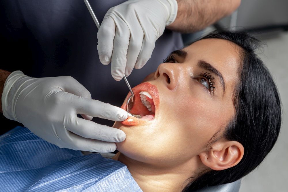 Female client with the mouth open while a dentist with gloves and tools examine her in a clinic. Client with the mouth open while a dentist examine her in a dental clinic
