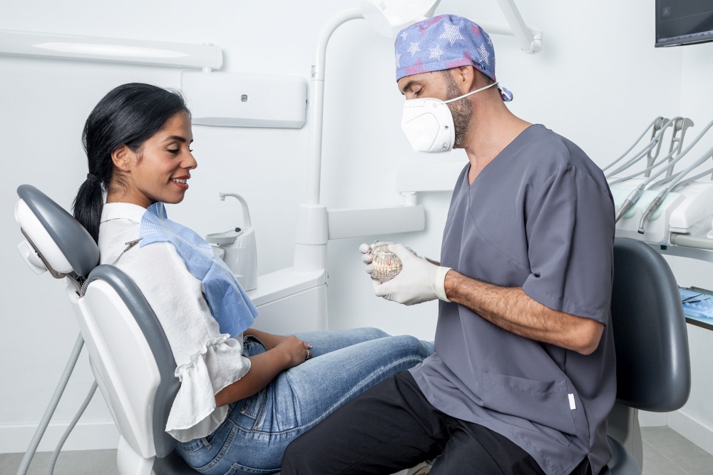 Male dentist showing a dental mould to a female patient sitting in a chair in a dental clinic. Dentist showing a dental mould to a patient sitting in a dental clinic.