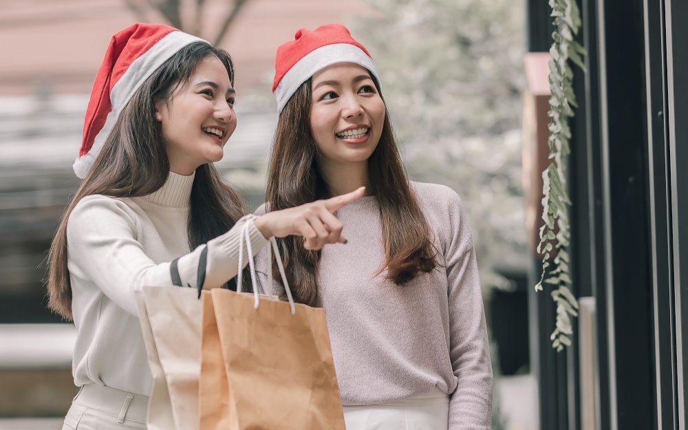 Two lovely women holding bags while doing window shopping at department store in Christmas season. New Year Celebration and Sales Discount Concept.