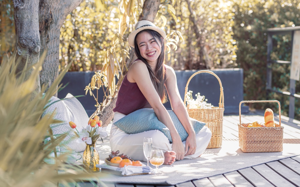 Asian beautiful woman wearing hat, smiling, going picnic and sitting in the garden. Lifestyle and Travel Concept.
