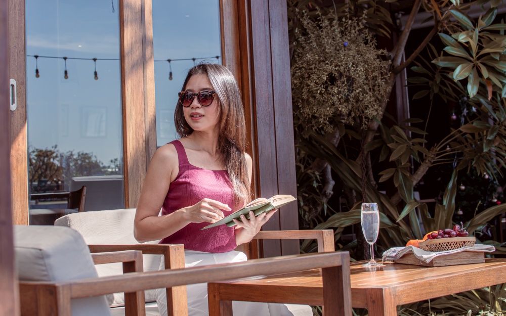 Asian beautiful woman wearing sunglasses, reading book and relaxing. Lifestyle and Travel Concept.