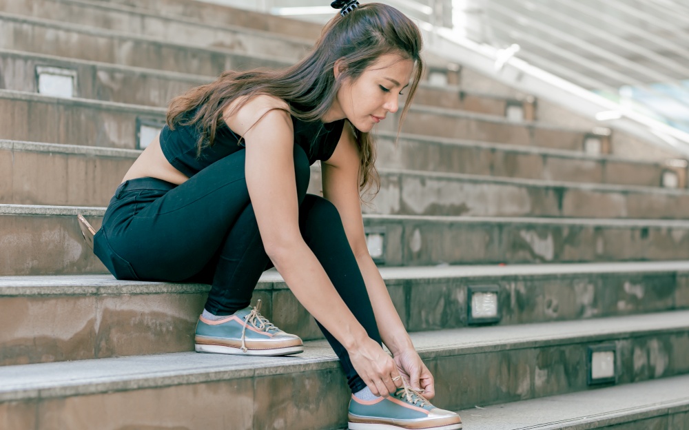 Asian healthy woman wear sport bra and tie shoelaces while sitting on stairs outdoor. Sport and Lifestyle Concept.