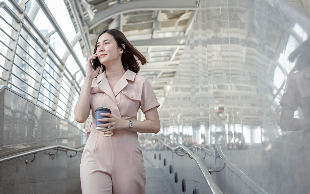 Asian business woman wearing formal pink suit holding tablet and coffee cup outside in the morning during going to work