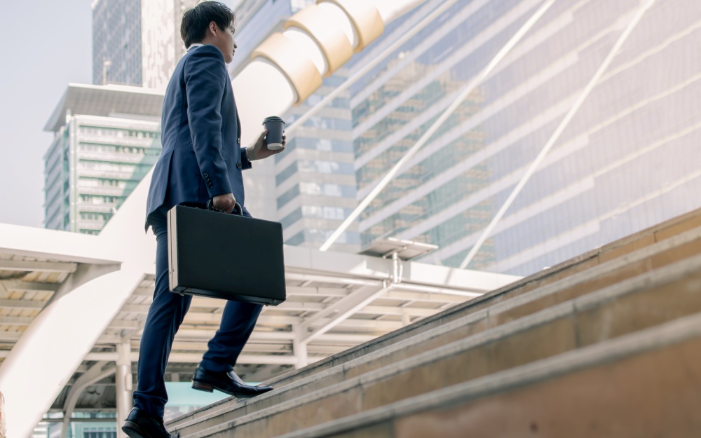 Focusing on business man wearing blue formal suit, holding briefcase, hurry and rush running on the steps while going to work in the early morning