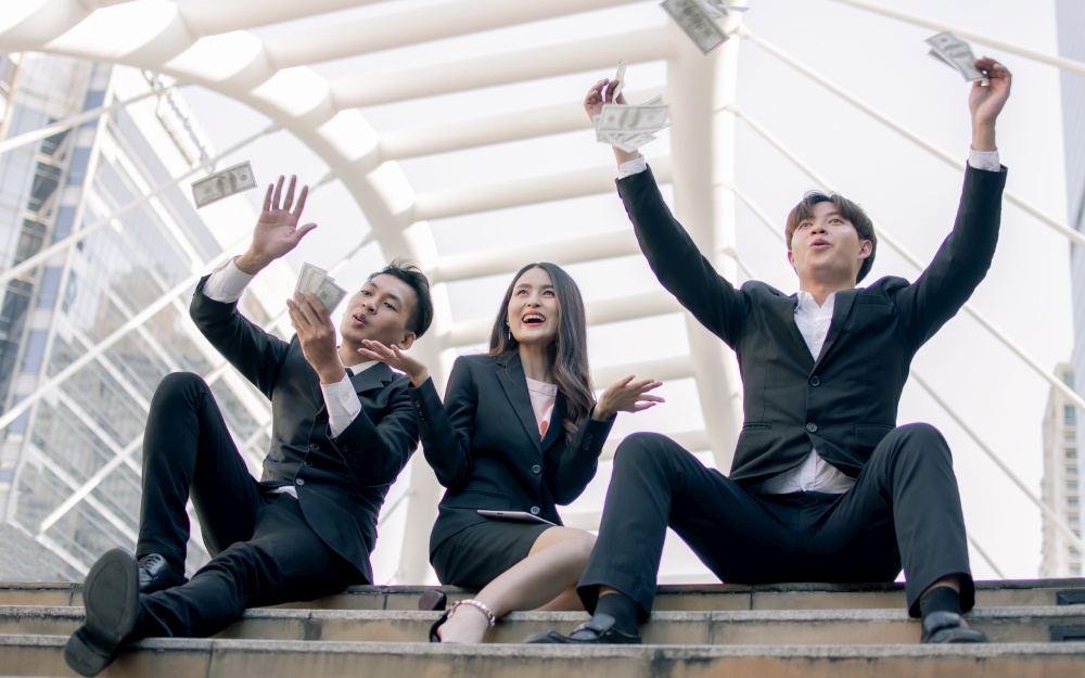 Asian rich business men and woman are very happy while sitting on stairs with a lot of money