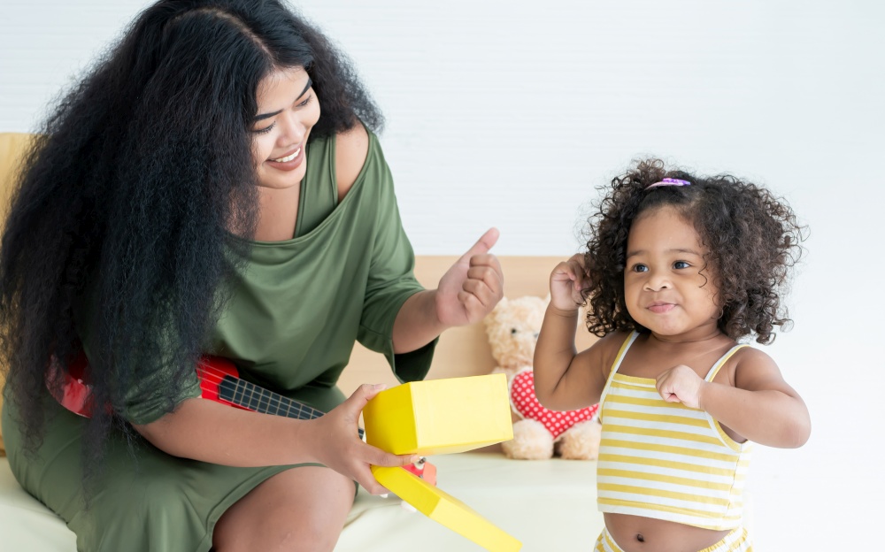 African black mother with afro hair giving gift box to her little daughter in living room at home for celebrating birthday. Education and Family Concept.