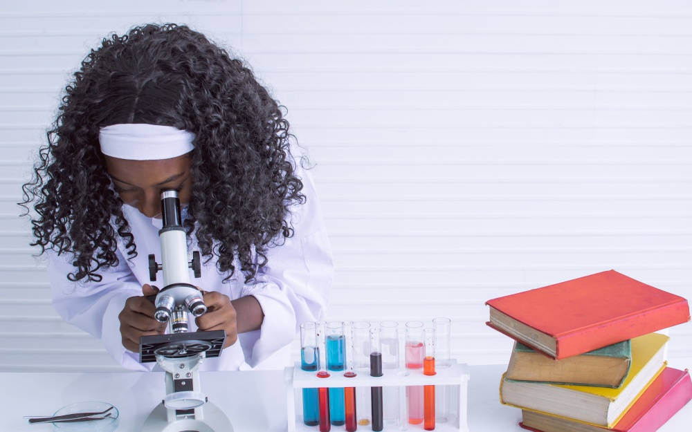 African black girl studying science and using microscope in classroom at school. Education and diversity concept.