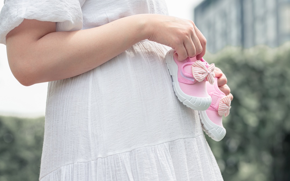 Pregnant woman holding pink girl&rsquo;s shoes while standing in garden