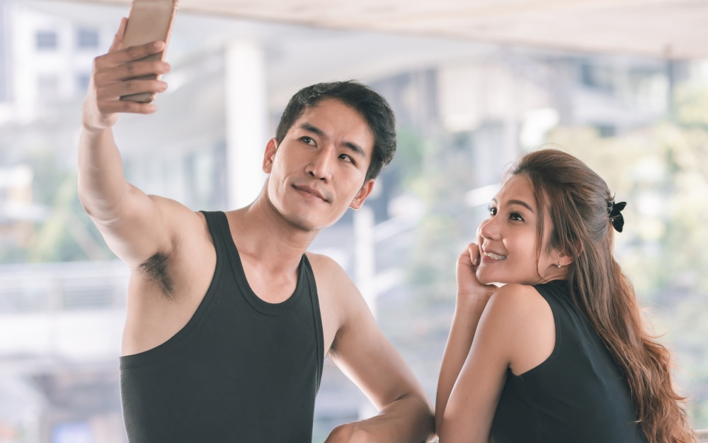 Asian sportive man and woman using mobile phone to take selfie. after doing exercise. Sport and Technology Concept.