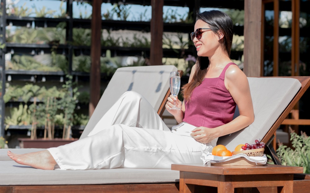 Asian beautiful woman waring sunglasses and drinking wine while taking rest outdoor on vacation. Travel and Summer Concept.