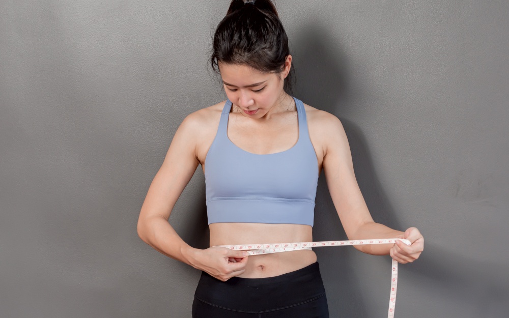 Portrait of Asian healthy, beautiful and sportive woman using tape to measure her waist after exercising and diet