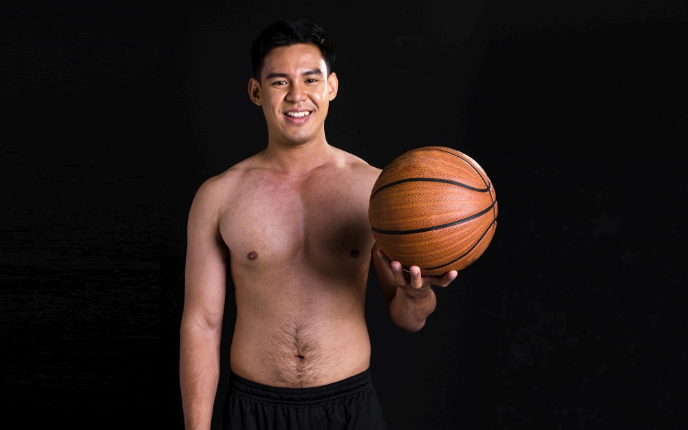 Portrait of asian young muscular man standing and holding basketball on black background with copy space. Healthy Concept.