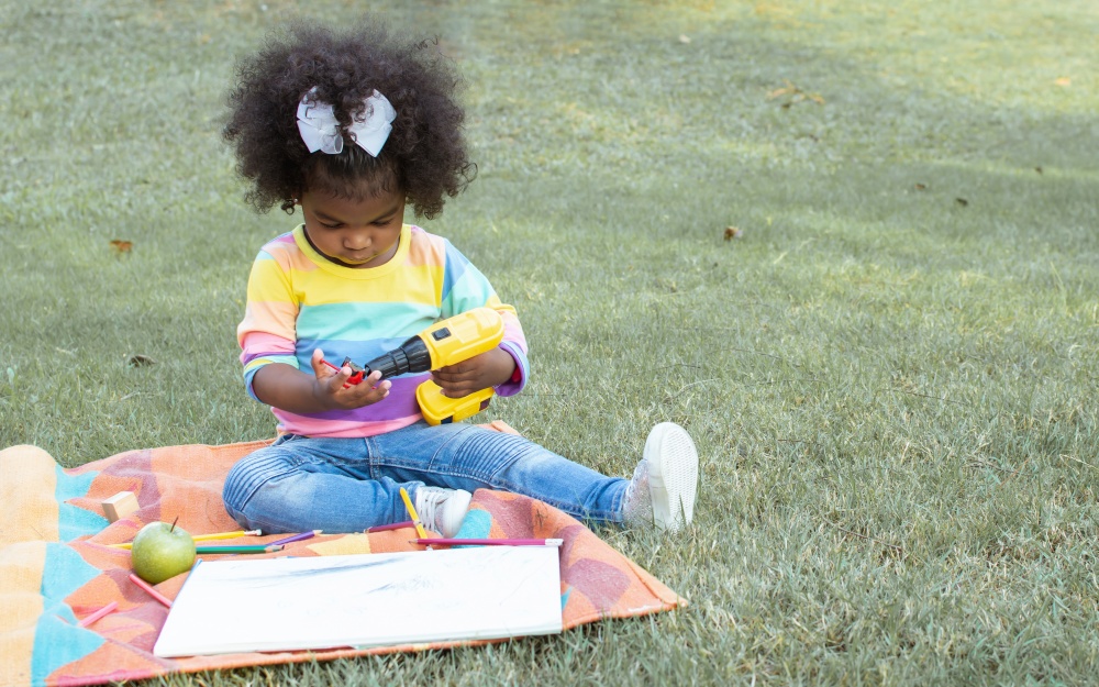 A little African girl wearing colorful shirt is playing in backyard. Education and Lifestyle Concept.