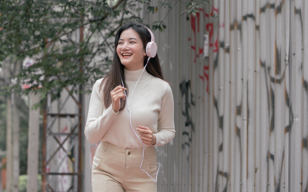 Asian pretty woman smiling, wearing headphone to listen music and running beside the street in the winter morning. Lifestyle Concept.