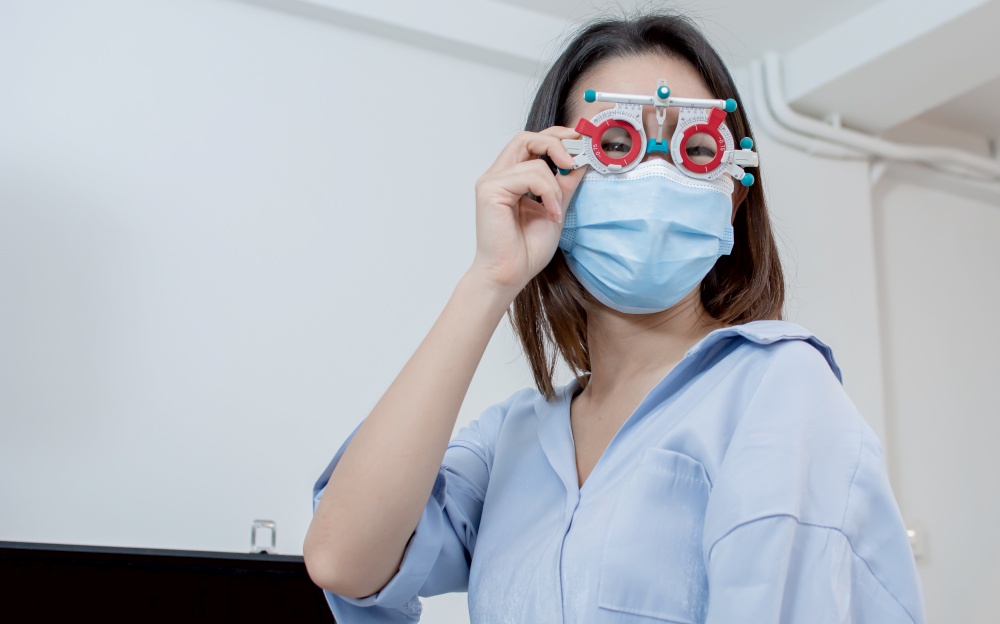 Portrait of asian beautiful young woman wearing mask to protect virus and doing eyesight test in optical lab