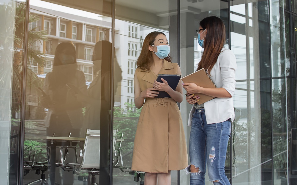 Business women are walking outside and talking together while wearing masks to protect virus. New Normal and Working concept.