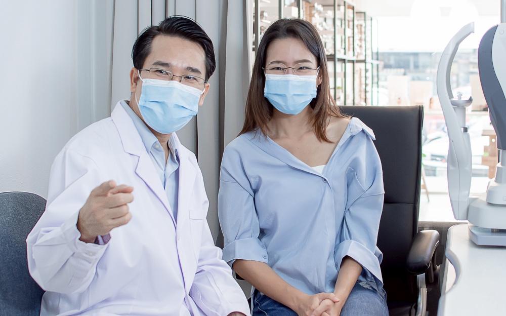 Asian young woman wearing mask to protect virus and consult Ophthalmologist about her short eyesight while trying glasses in optical lab