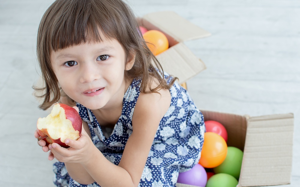A caucasian little girl is happy while smiling and eating an apple