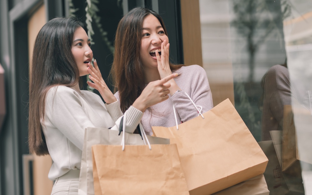 Two beautiful asian women surprising, holding paperbags and doing window shopping. Winter Season, Friendship and Sales Discount Concept.