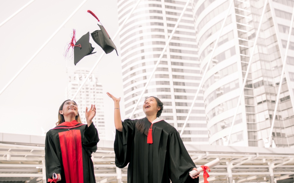 Two asian female students wearing uniform, smiling with happiness and throwing caps  after graduation. Education Concept.