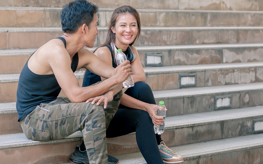 Asian sportive man and woman drinking water and talking together after doing exercise. Health, Sport and Lifestyle Concept.