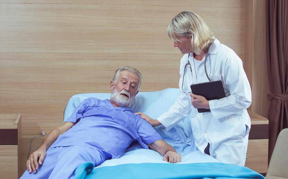 A senior female caucasian doctor taking care and examining an aging male patient while staying on bed at hospital
