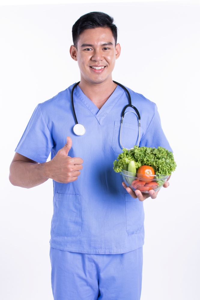 Asian young male doctor or nutritionist smiling and and holding a bowl of vegetables while standing on white background with copy space. Medical and Nutrition Concept.