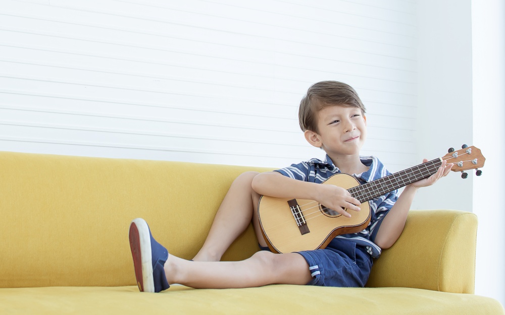 Portrait of caucasian little boy is happy while playing guitar on yellow sofa in living room at home