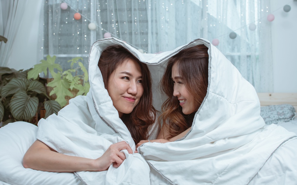 Two asian women laying down under blanket and staying on bed at home showing LGBT Concept.