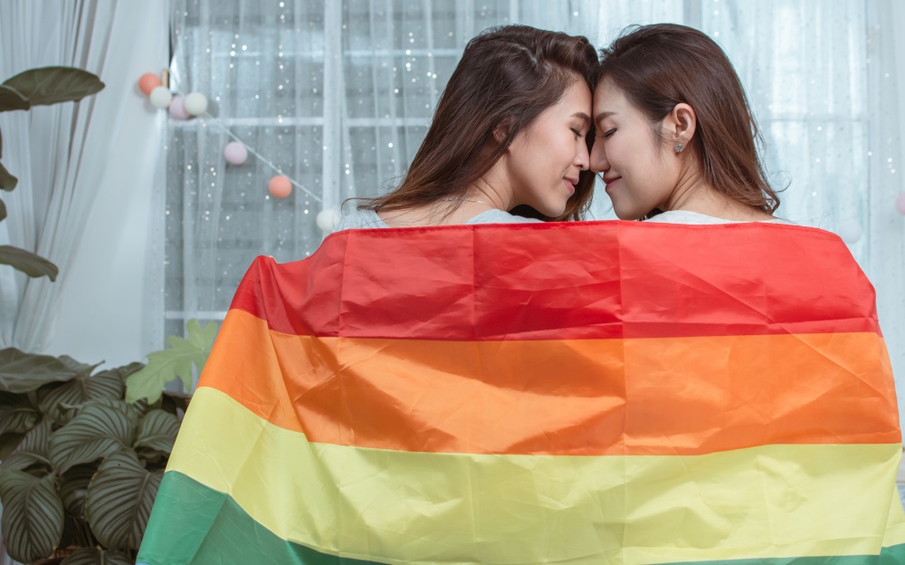 Portrait of two asian women with rainbow flag and standing in a house showing LBGT concept.