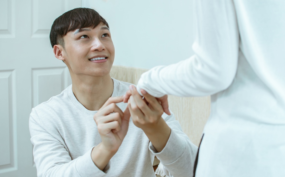Asian handsome man giving a propose for marriage and wearing a ring to his girlfriend. Valentine and Love Concept.