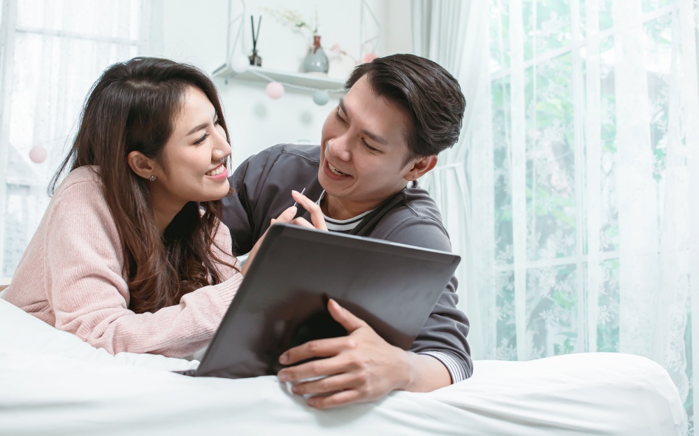 Asian adult cute couple doing online shopping in the internet by using laptop at home and making payment by credit card. Technology, Finance and New Normal Concept.