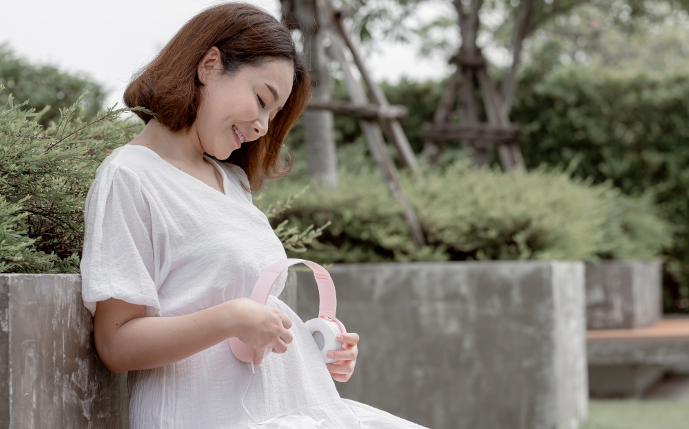 Asian beautiful pregnant mother put headphone on her stomach to let her baby listen music. Mother, Baby and Pregnancy Concept.