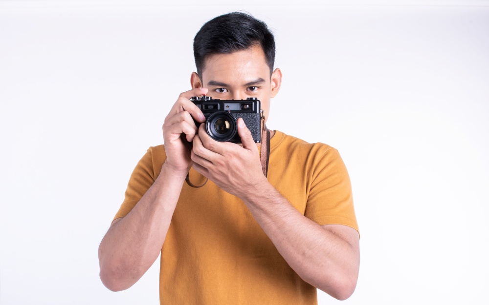 Asian handsome man holding camera and wearing casual shirt for traveling, standing on white background