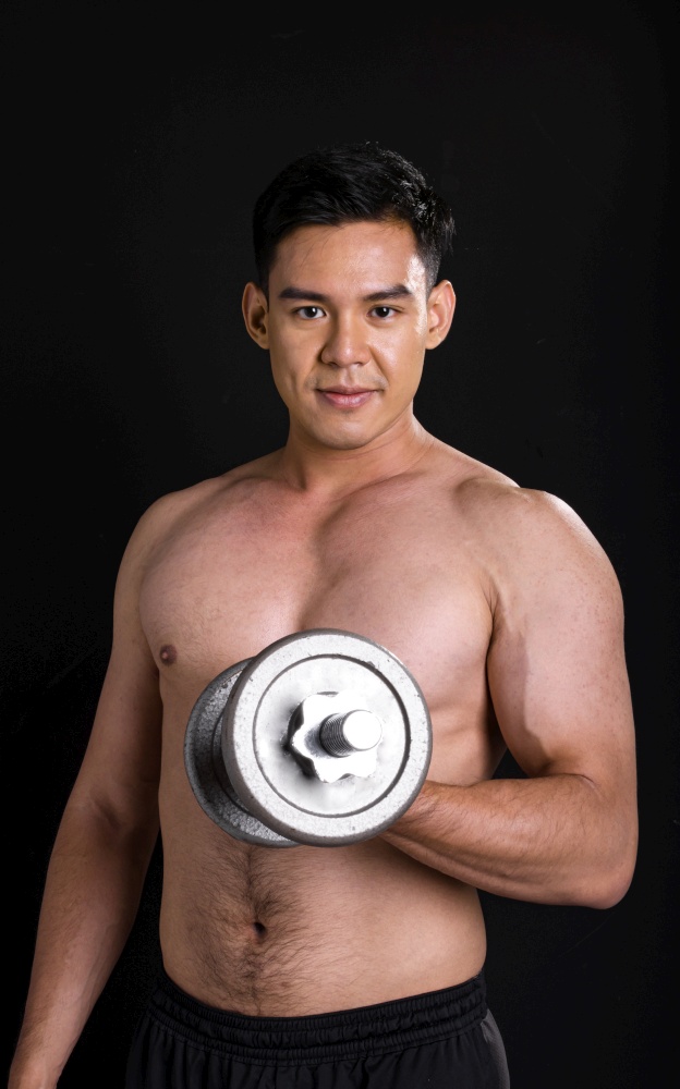 Portrait of asian young muscular man standing and lifiting dumbbell on black background with copy space. Healthy Concept.