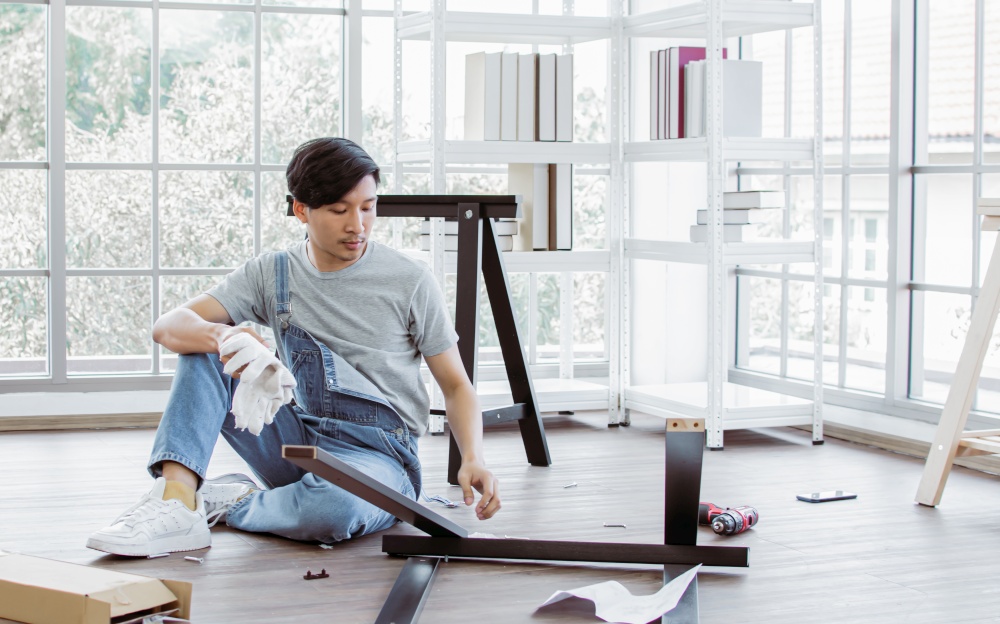 An asian handsome man is making an assembly of a furniture at home. Interior design and DIY Concept.
