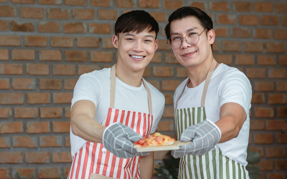 Portrait of two Asian handsome men cooking and holding a dish of pizza. Lifestyle and LGBT Concept.